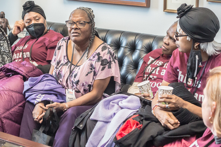 Several people sit in the office of a member of Congress. Four people are on couches and two people are in arm chairs. They wear AIDSWatch shirts that read, "This is what an HIV advocate looks like."